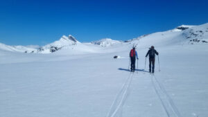 To personer som går på ski i snødekket landskap. Fjell i bakgrunnen 