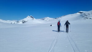Two people skiing in a snowy landscape. Mountains in the background